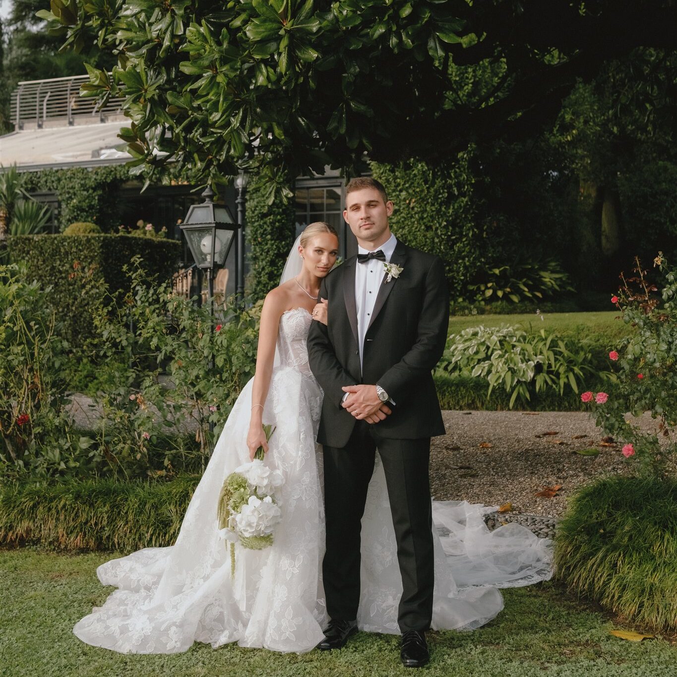 Bride in ballgown and groom posing in editorial way in lush garden